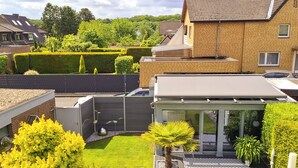 A residential property with a fenced backyard, a small patio area with a palm tree, and a modern house with a sloped roof. - Modern vacation apartment in Dülmen: close to the city with a balcony view of the countryside (Dülmen)