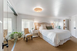 A bedroom with a bed, bedside table, lamp, chair, and potted plants. - Casa Alma del Mar | Hot Tub + Walk to Beach (Santa Barbara)