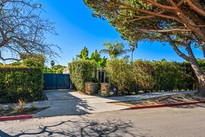 A gated driveway leading to a building with a stone wall and a palm tree. - Casa Alma del Mar | Hot Tub + Walk to Beach (Santa Barbara)