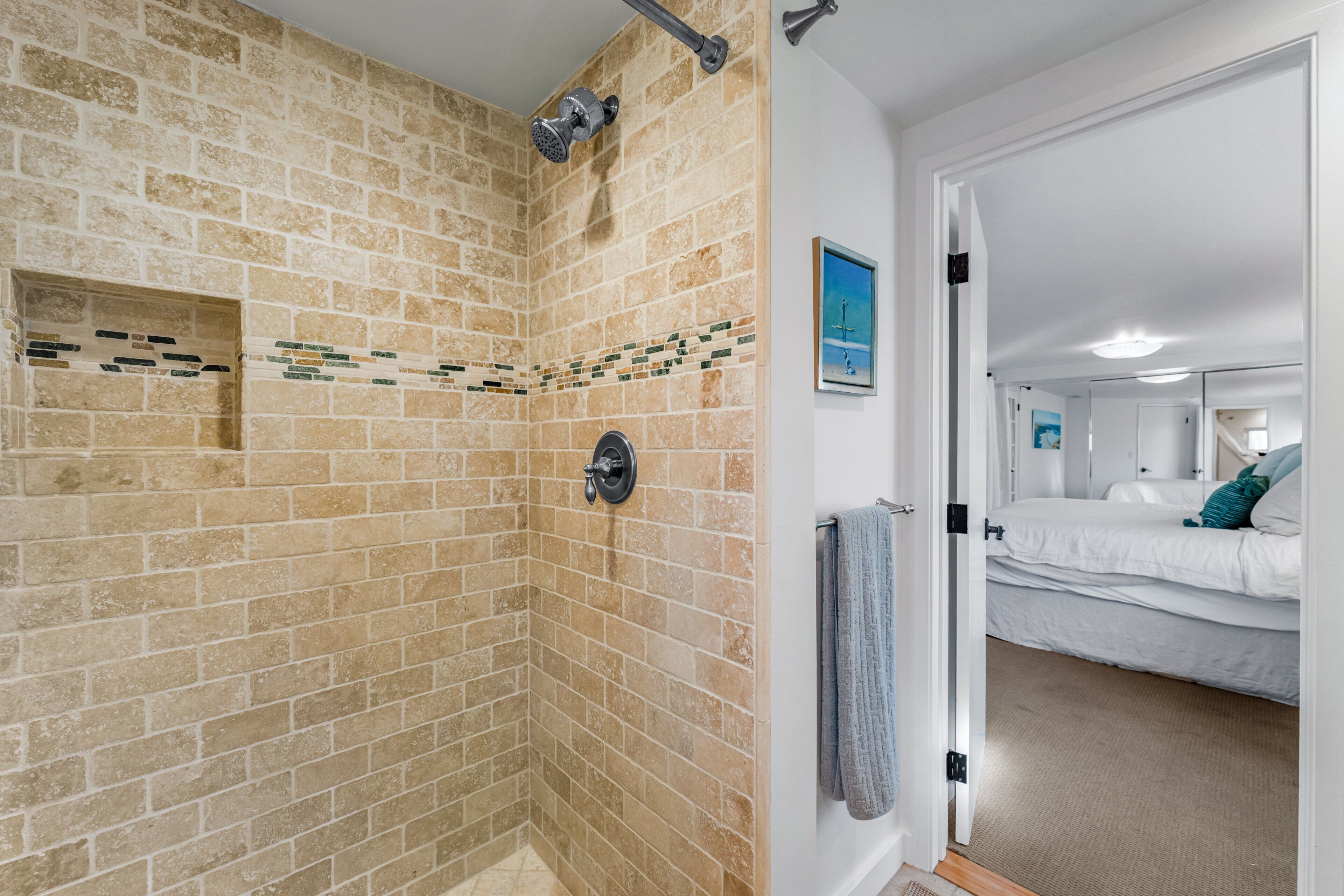 A bathroom with a shower, a towel rack, and a door leading to a bedroom with a bed and a nightstand.