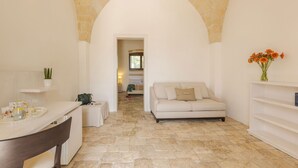 Una habitación amplia con piso de piedra, un sofá blanco, una mesita con bandeja y una planta en maceta.