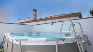 Una piscina elevada con escalera, rodeada de un muro blanco, y una chimenea al fondo.
