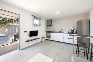 A modern kitchen with a flat-screen TV, stainless steel appliances, and a sliding glass door leading to an outdoor area. - Apartment with Private Pool, Barbecue, Wi-Fi and Air Conditioning (Conil de la Frontera)