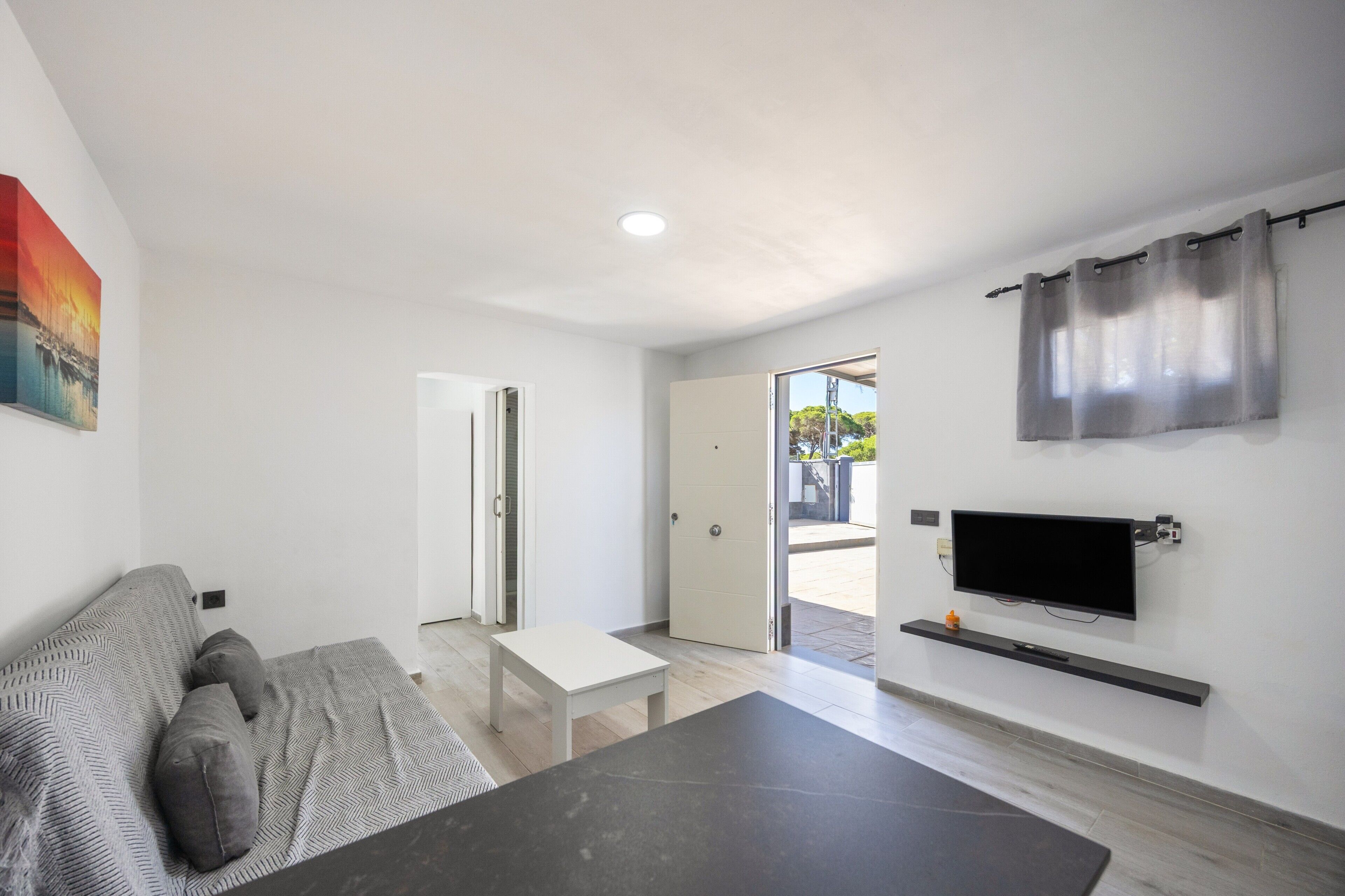 Una sala de estar moderna con un sofá, una mesa de centro, un televisor montado en la pared y una puerta que da a un espacio exterior.