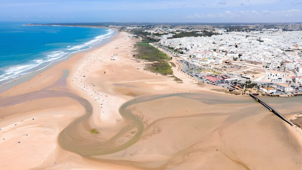 Un paisaje costero con playa, un río serpenteante y una zona urbana densa con edificios.