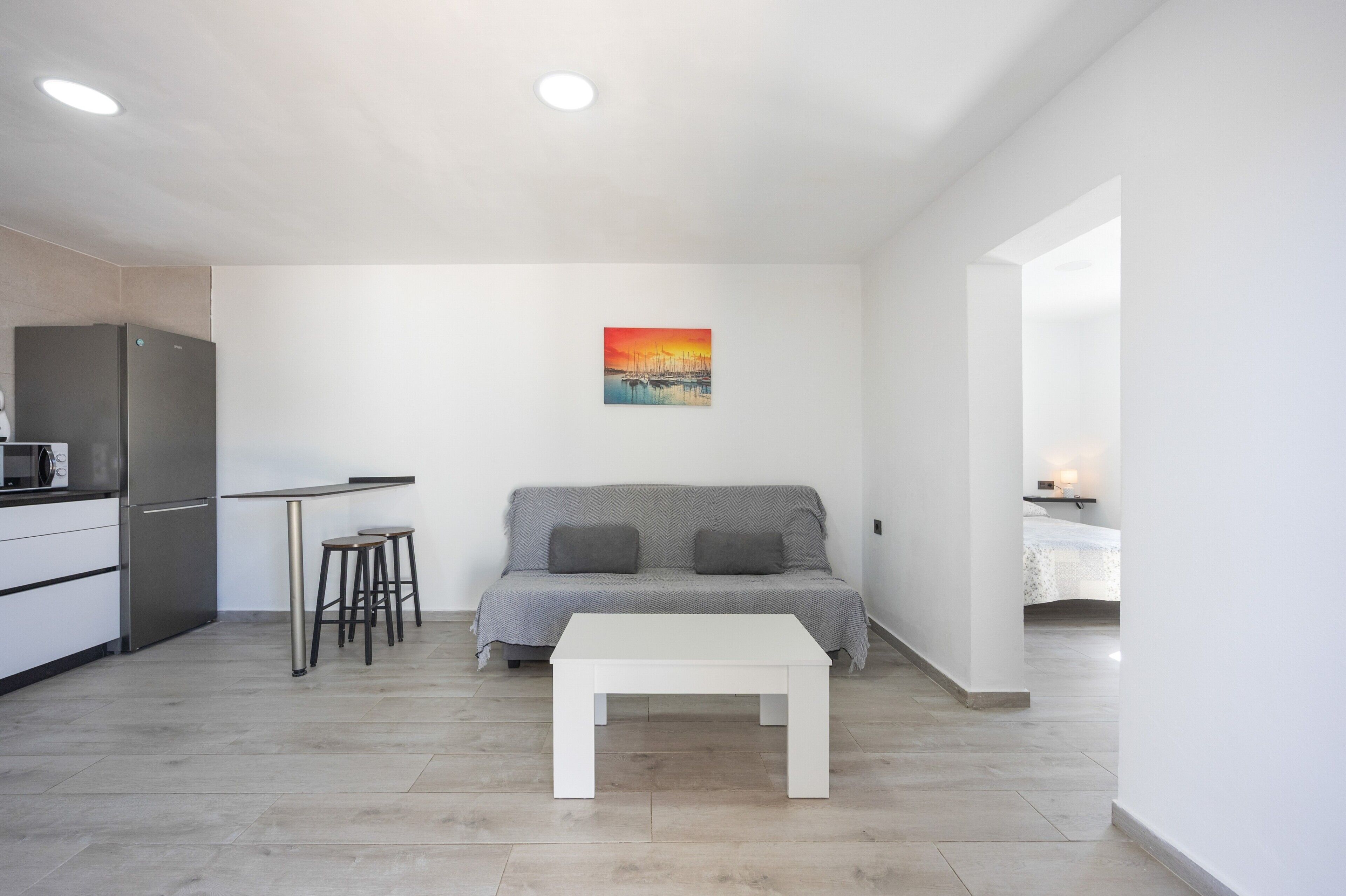 Un ambiente moderno e minimalista con angolo cottura, divano e un quadro appeso al muro.