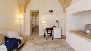 A room with a stone floor, a white sofa, a desk with a chair, and a small plant on a shelf.