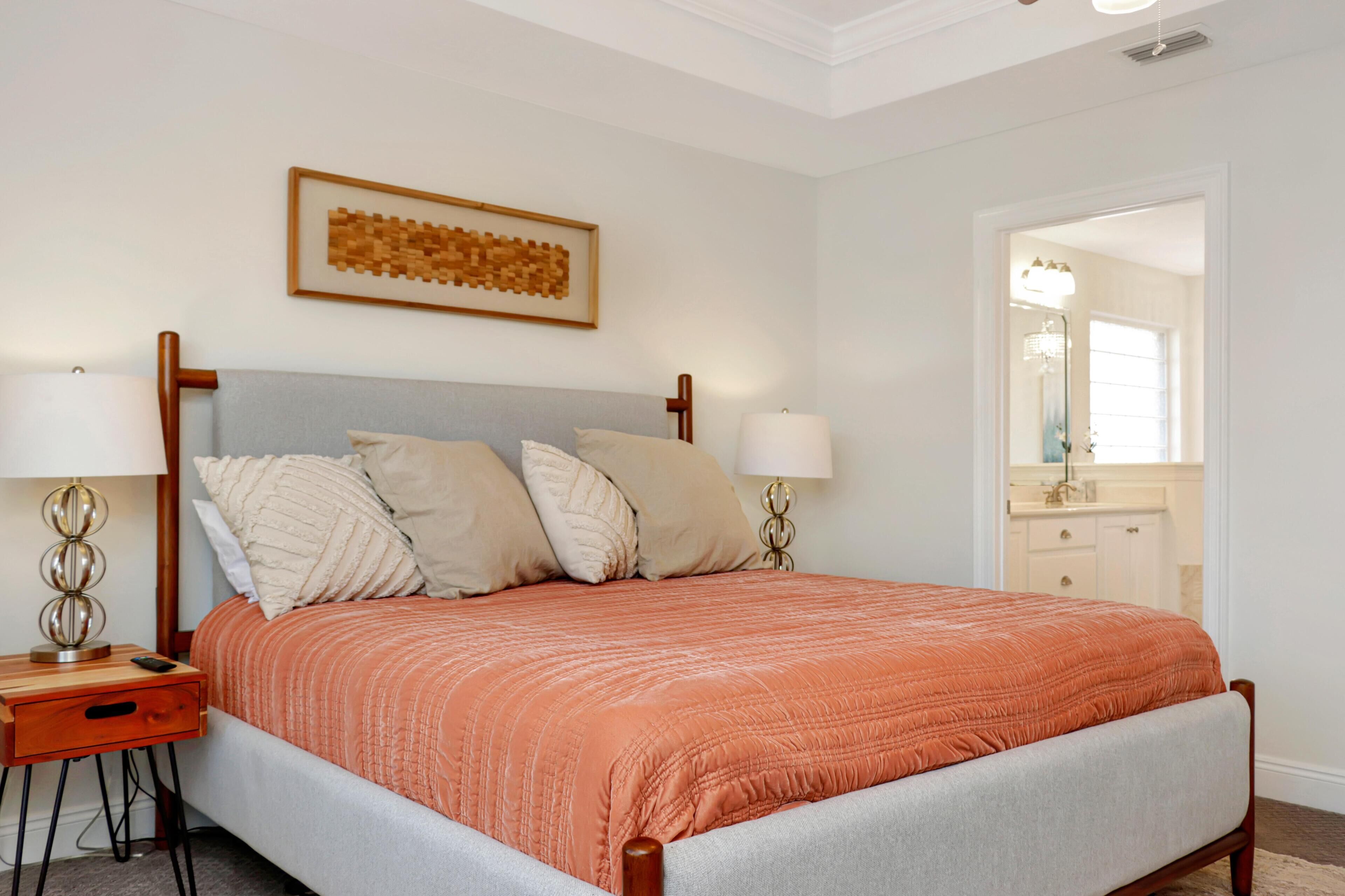 A bedroom with a bed, nightstands, a wall-mounted artwork, and a door leading to another room.