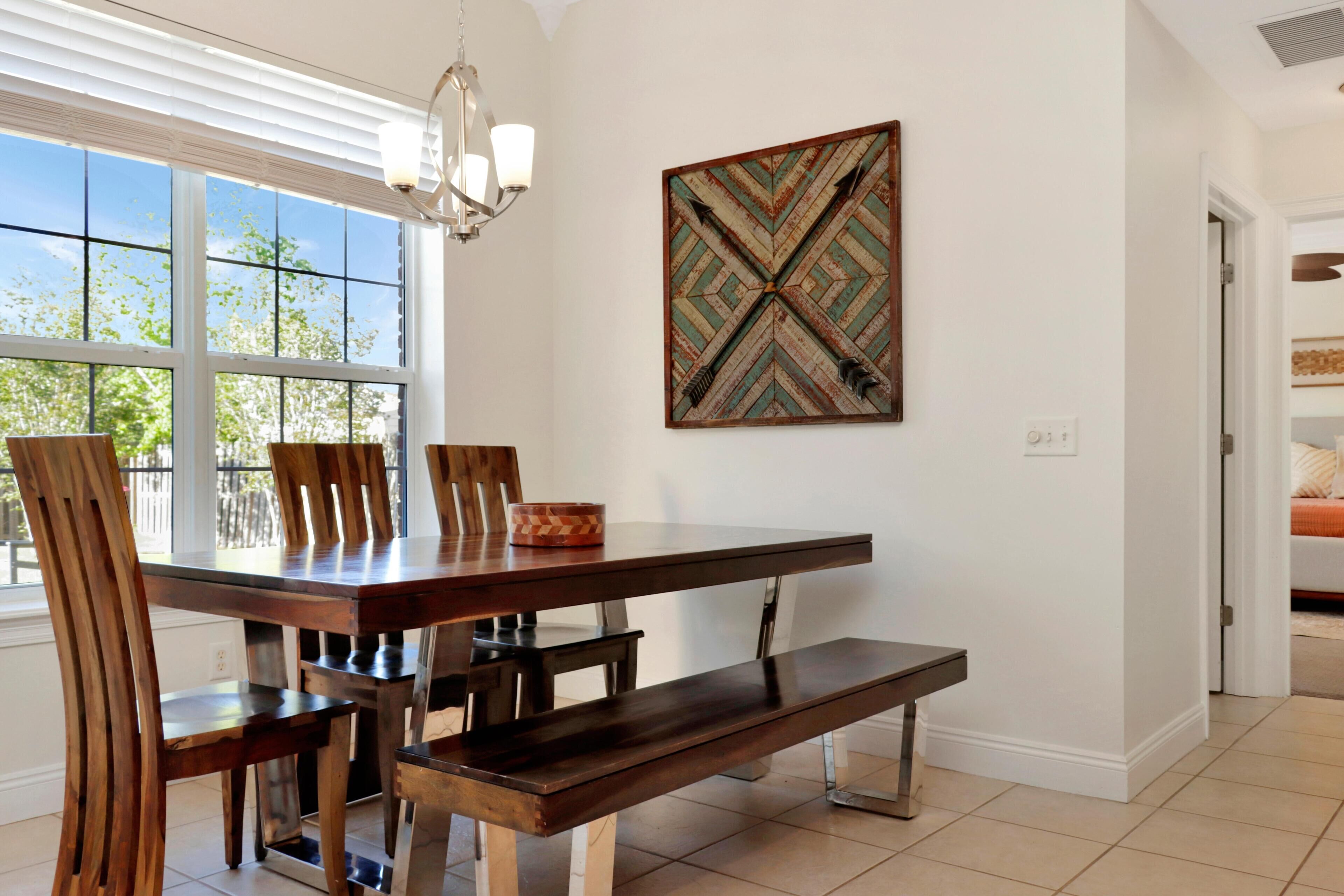 A dining area with a wooden table, chairs, a bench, a chandelier, and a wall-mounted artwork.