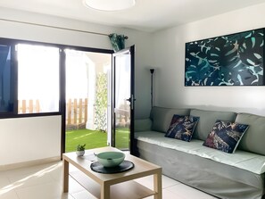 Een moderne woonkamer met een bank, een tafel met een schaal, een schilderij en uitzicht op een tuin door een schuifdeur.