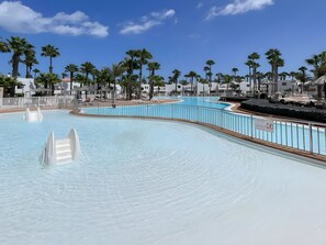 Ein Schwimmbecken mit Holzterrasse, Palmen und einem weißen Zaun.