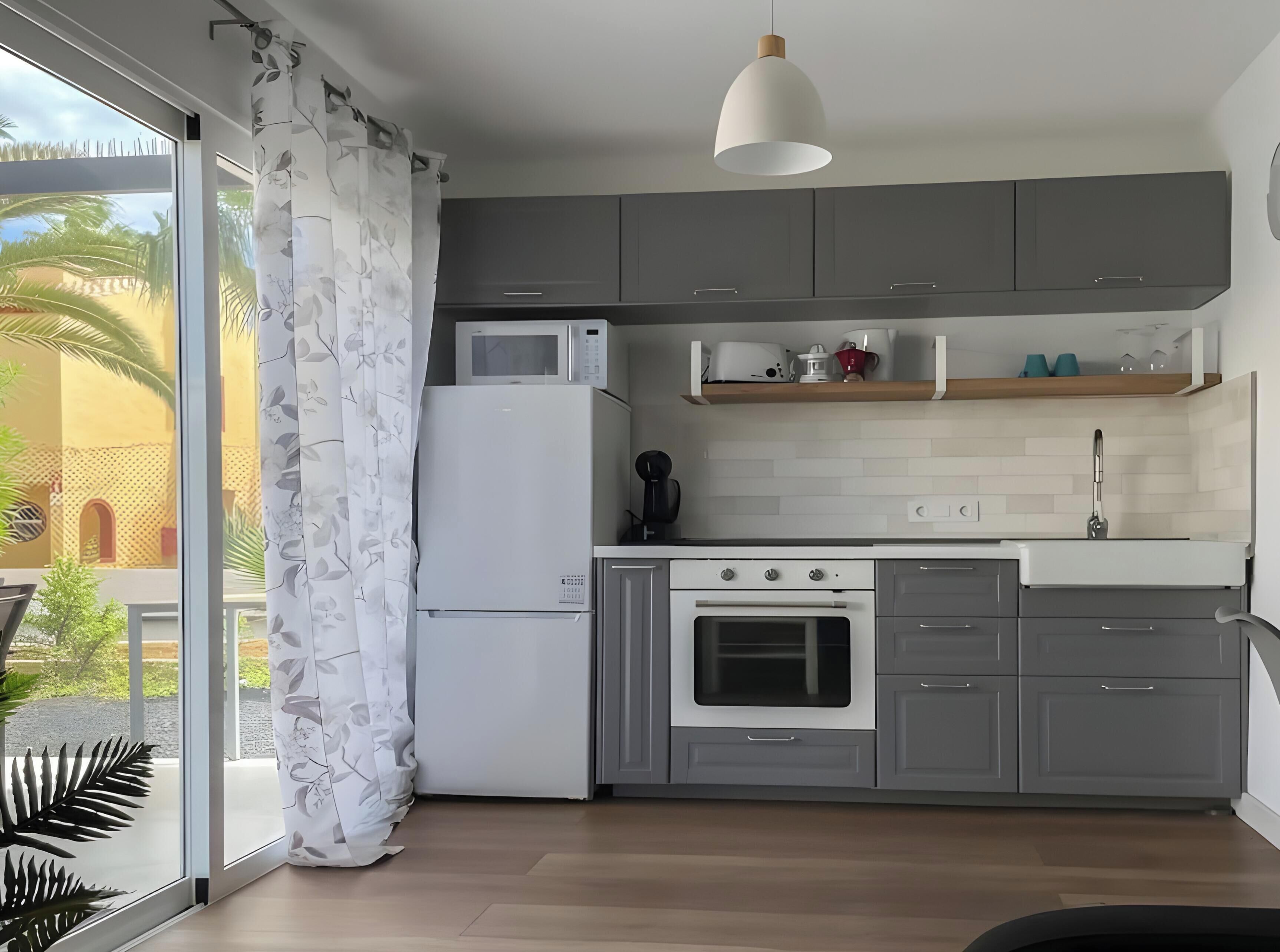 Una cocina moderna con armarios grises, un refrigerador blanco, un microondas, una cafetera y un lavamanos.