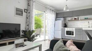 Ein modernes Wohnzimmer mit Flachbildfernseher, einer Couch, einem Couchtisch und einer Küchenzeile mit Mikrowelle, Backofen und Schränken.