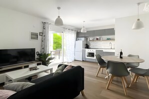 Ein modernes Wohnzimmer mit Flachbildfernseher, einer Couch, einem Esstisch mit Stühlen und einer Küchenzeile inklusive Mikrowelle, Backofen und Schränken.