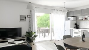 Ein modernes Wohnzimmer mit Flachbildfernseher, einer schwarzen Couch und einem Essbereich mit Tisch und Stühlen.