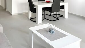 Uma sala de jantar moderna com uma mesa branca, cadeiras pretas e um quadro com barcos à vela.