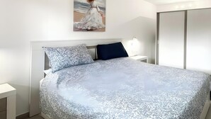 Quarto com cama grande, mesa de cabeceira, luminária na parede, guarda-roupa e pintura de uma mulher num vestido.