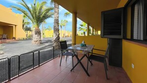 Uma varanda com mesa e cadeiras, uma palmeira e um edifício amarelo ao fundo.