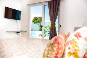 Una camera da letto con un letto, una TV a muro, una porta scorrevole in vetro che dà su una piscina e vista sull'esterno.