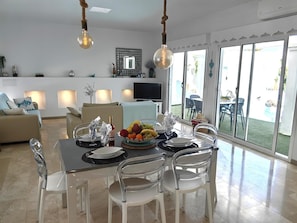 A dining area with a table set for four, a fruit bowl, and a bottle of wine. - Bahiazul Villa Opale by B-Rent Corralejo (La Oliva)