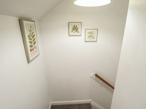 Una escalera con barandilla, un rellano alfombrado y tres ilustraciones botánicas enmarcadas en la pared.
