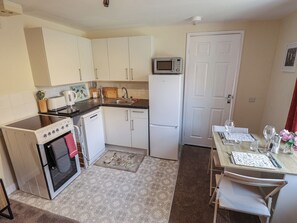 A compact kitchen with a stove, oven, microwave, sink, and a dining area with a table and chairs. - Goldfinch (Spilsby)