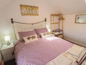 A neatly made bed with checkered bedding, a bedside lamp, a wooden ladder, and a painting on the wall. - Goldfinch (Spilsby)