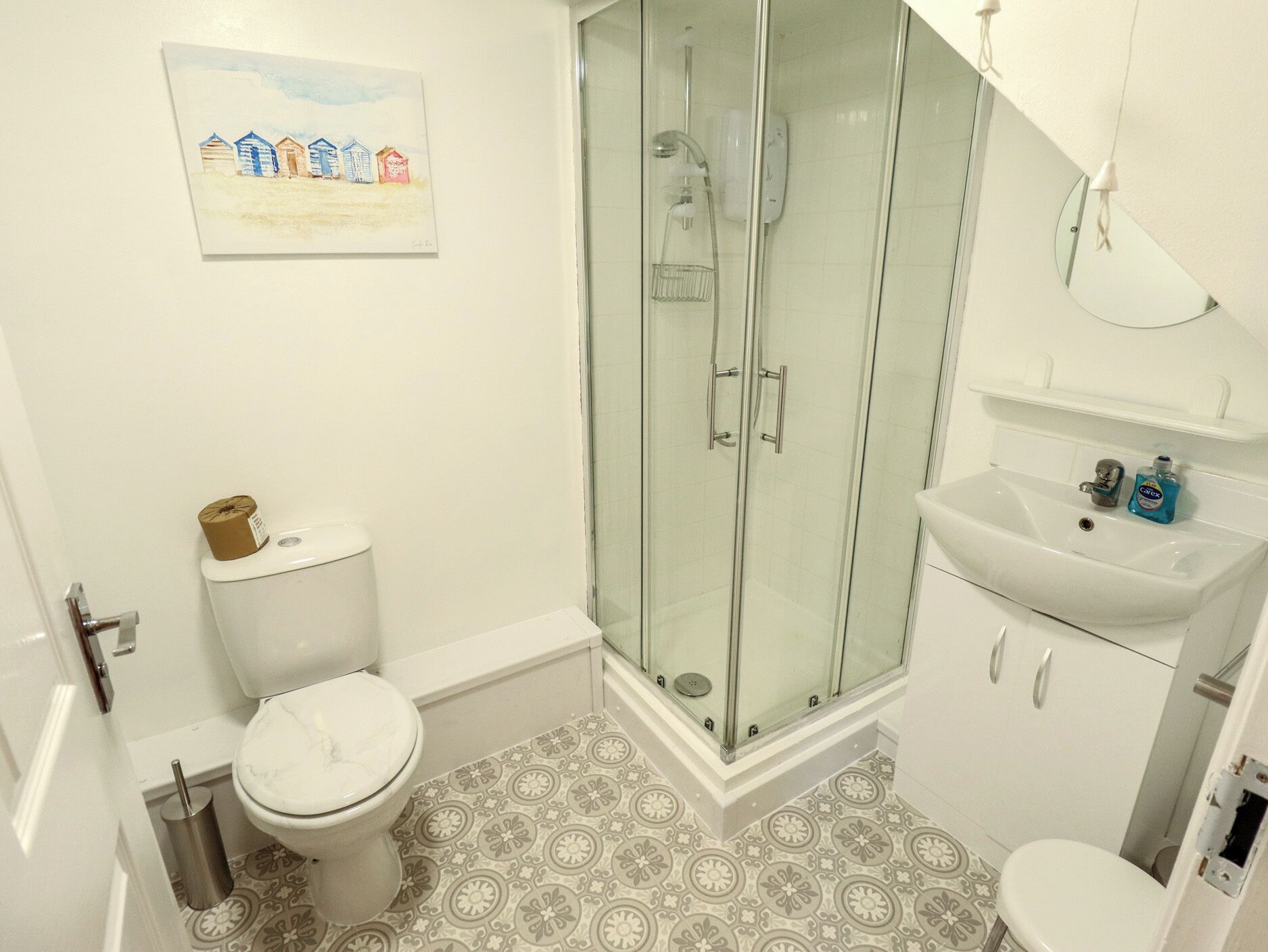 Un baño con inodoro, ducha con cerramiento de vidrio, lavamanos y baldosas de suelo con diseño.