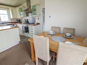 A compact kitchen with white cabinets, a stove, and a dining area with a wooden table and four chairs. - Plot 34 (Carlisle)