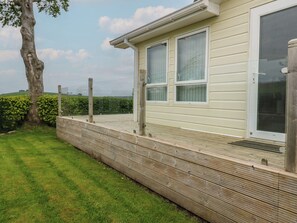 A house with a wooden deck, large windows, and a tree in the background. - Plot 34 (Carlisle)