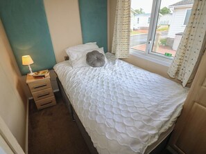 A small bedroom with a bed, a nightstand, a lamp, and a window with curtains. - Plot 34 (Carlisle)