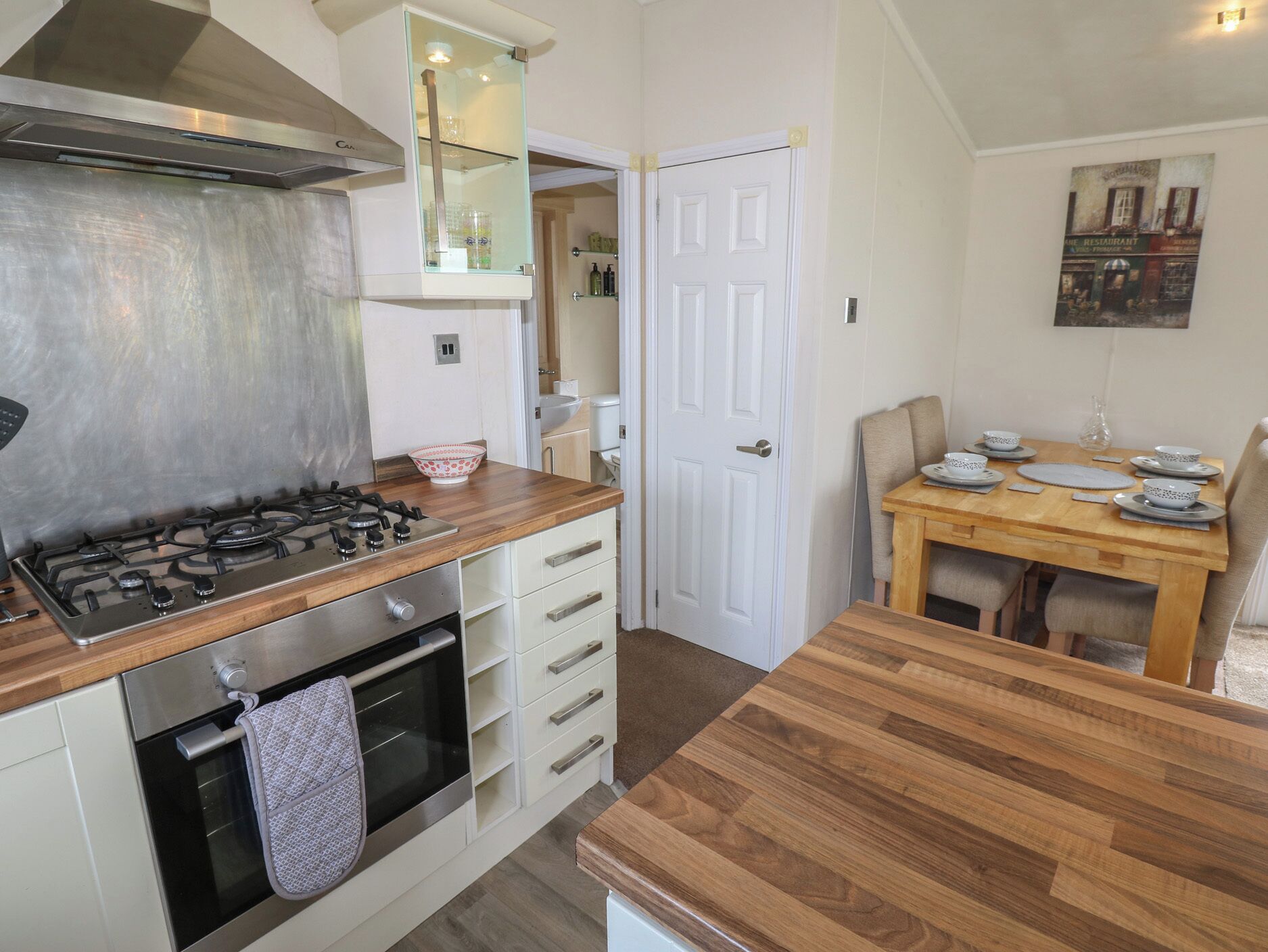 Una cocina con estufa a gas, horno y encimera de madera. Hay un comedor con mesa y sillas.