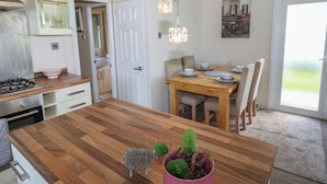 Uma cozinha com uma ilha de madeira, uma mesa de jantar com cadeiras, um lustre pendurado e uma porta que dá para um banheiro.
