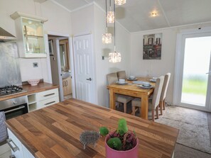 A kitchen with a wooden island, a dining table with chairs, a hanging light fixture, and a door leading to a bathroom. - Plot 34 (Carlisle)