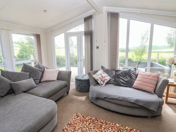 A spacious living room with two grey sofas, a round ottoman, and a patterned rug. - Plot 34 (Carlisle)