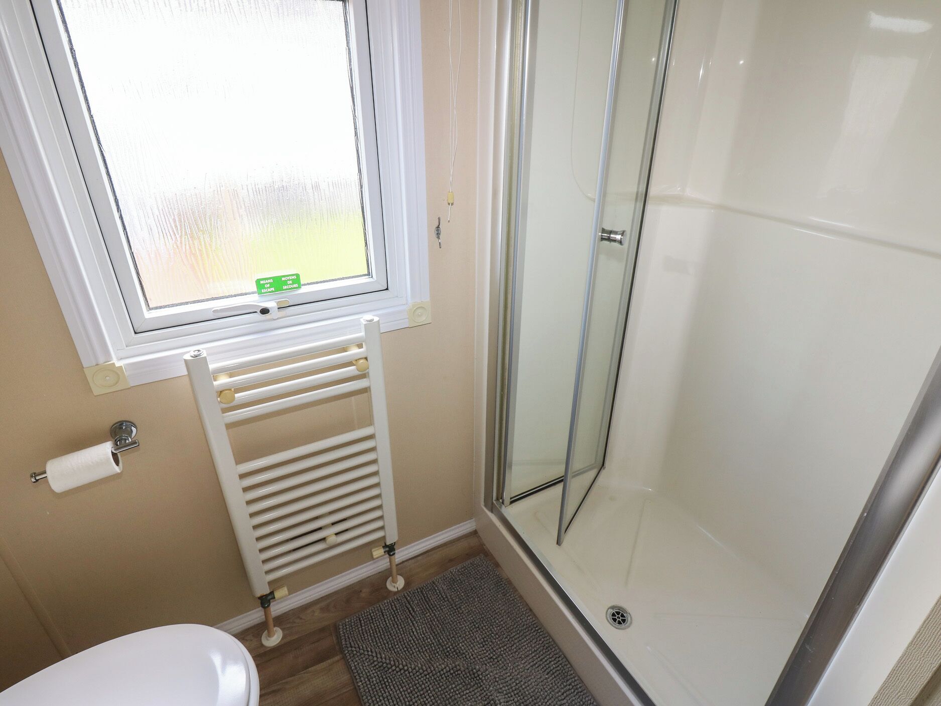 A bathroom with a toilet, a glass shower enclosure, a window, and a radiator.