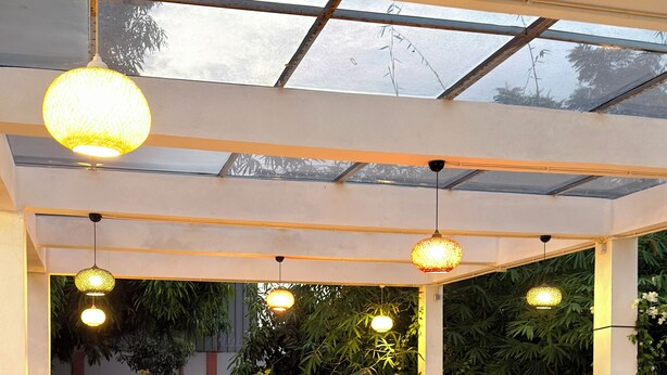 A modern outdoor seating area with wooden flooring, wicker chairs, and hanging pendant lights.