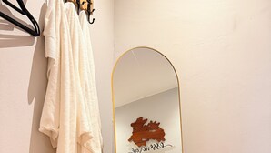 A room with a wooden floor, a white bed, a large mirror, and a towel hanging on a hook.