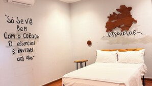 A bedroom with a bed, a wall-mounted air conditioner, a wooden floor, and a wall with a quote and a wooden map.