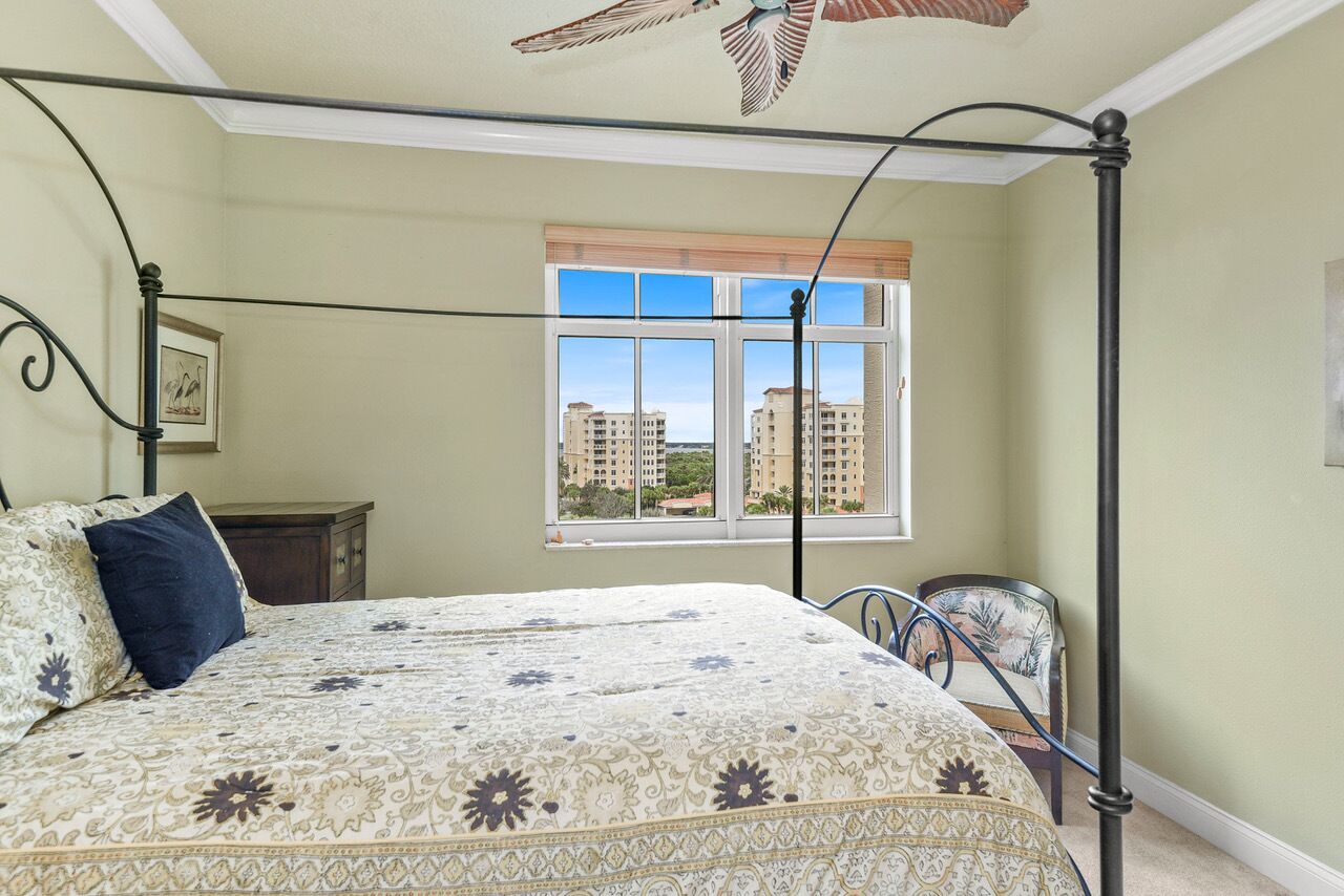 Une chambre à coucher avec un lit à baldaquin, une fenêtre donnant sur des immeubles, une chaise et une petite table.