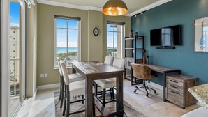 Ein Zimmer mit Esstisch, Stühlen, Schreibtisch, Sessel, Fernseher und Blick ins Freie.