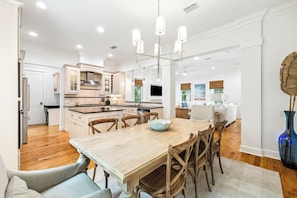 A modern kitchen with wooden cabinets, a central island, and a dining area with a wooden table and chairs. - Watersound Home w/ LSV and Community Pool (Watersound)