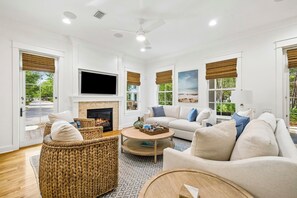 A spacious living room with a fireplace, a flat-screen TV, a sofa, and a wicker chair. - Watersound Home w/ LSV and Community Pool (Watersound)