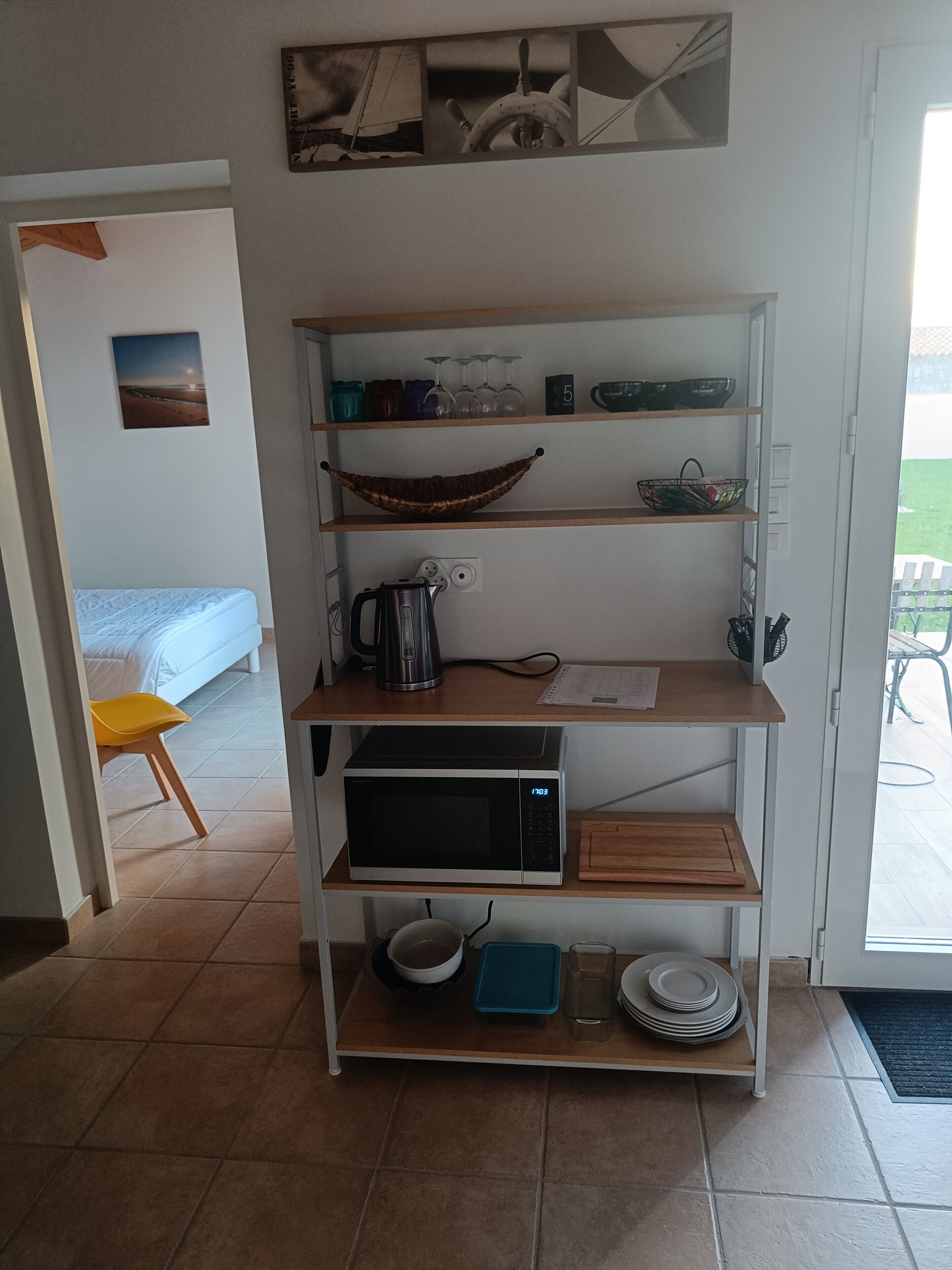 A kitchen area with a microwave, kettle, and various kitchen utensils on shelves.