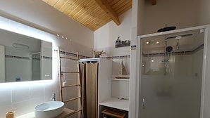 Une salle de bain moderne avec un grand miroir, un lavabo blanc, une cabine de douche et un plafond en bois.