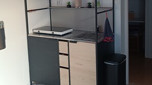 Une petite pièce comprenant un lit superposé, un bureau avec un ordinateur, une poubelle et une petite étagère avec des objets décoratifs.