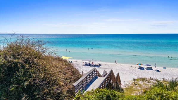 Ein Strand mit klarem, blauem Wasser, einer Holzpromenade und Strandstühlen.