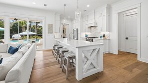 A modern kitchen with white cabinetry, a central island, and bar stools. - Retreat Close to Beachw/ Pool and Screened Porch (Santa Rosa Beach)