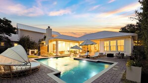 A swimming pool with lounge chairs and umbrellas, surrounded by a brick patio and a house with a metal roof. - Retreat Close to Beachw/ Pool and Screened Porch (Santa Rosa Beach)