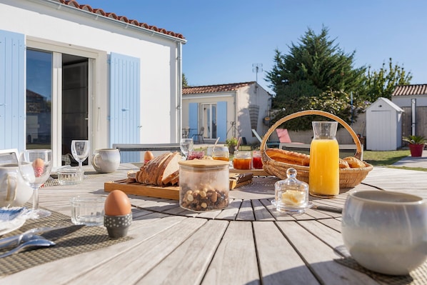 Un desayuno al aire libre con pan, huevos y bebidas sobre una mesa de madera.